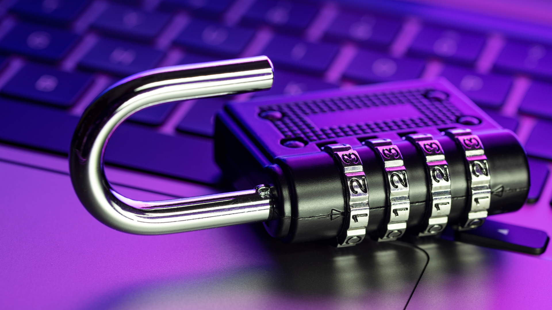 A 3-digit combo lock bathed in purple light sitting unlocked on a laptop keyboard.